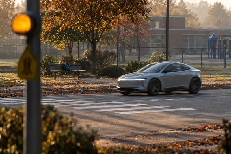 Driverless compact electric car blurs past a school crosswalk as an amber school-zone beacon flashes in morning light